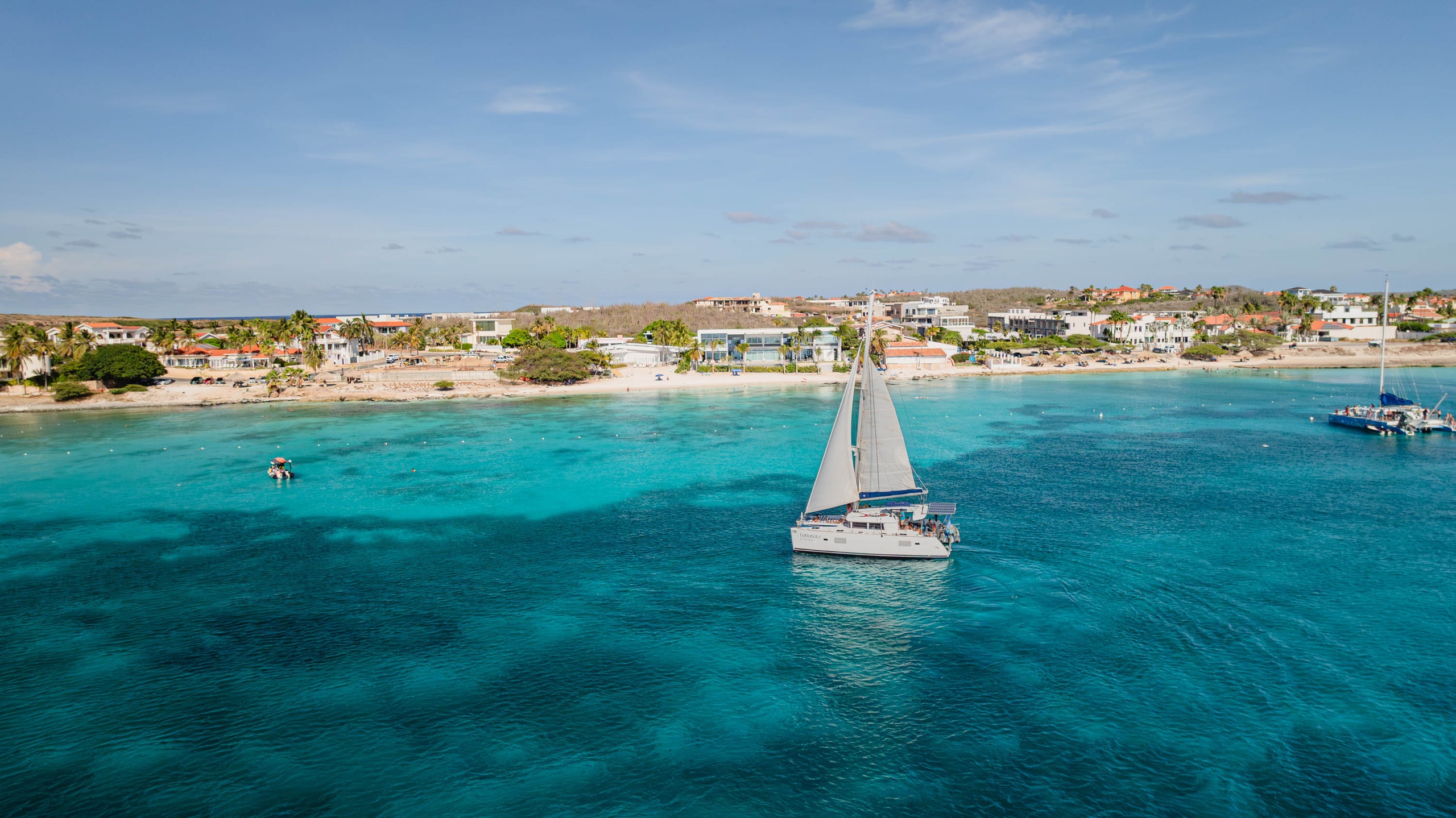 Sailboat on turquoise sea near a tropical island resort.