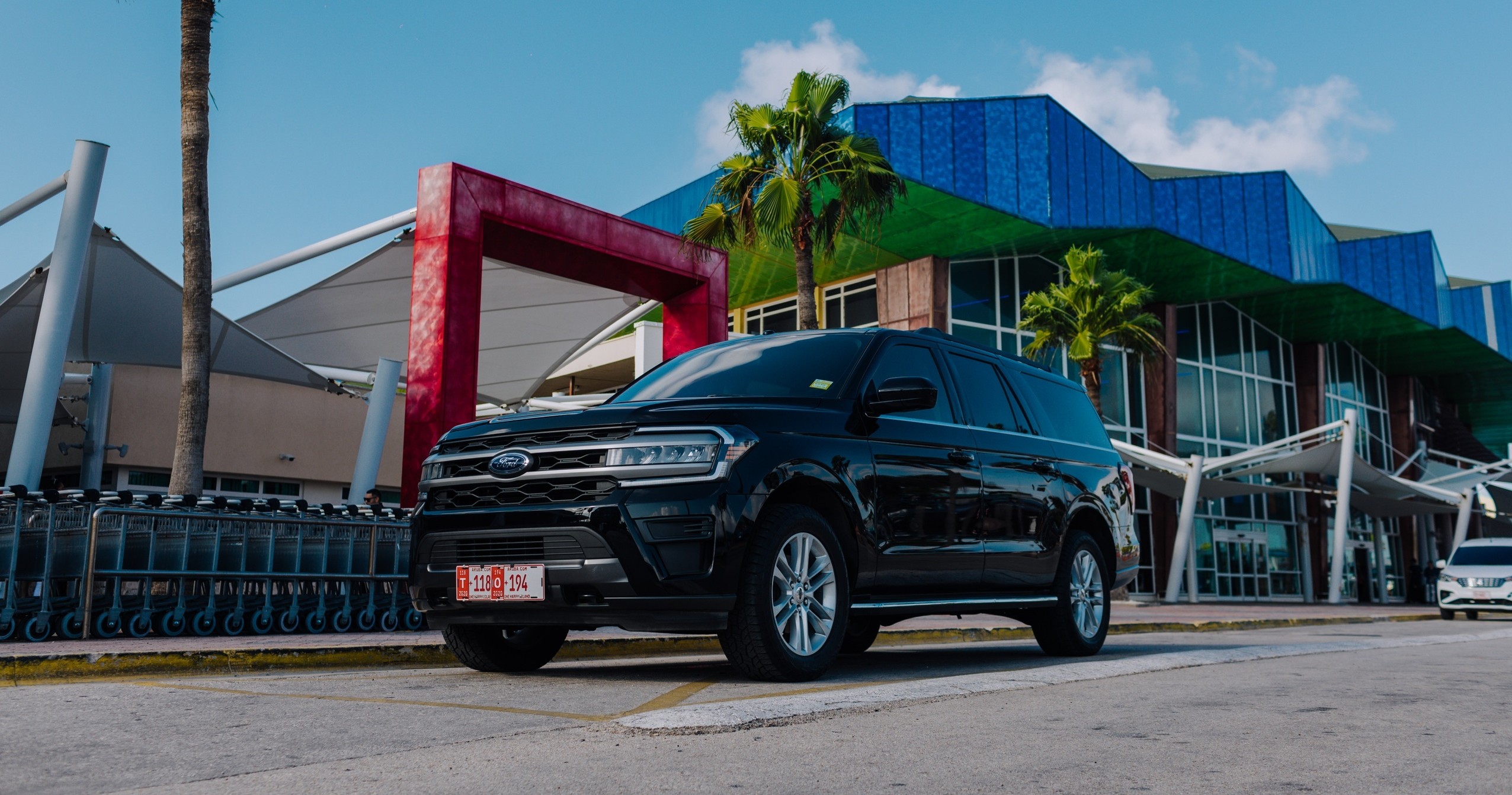 Black SUV parked outside a modern building with blue accents and palm trees.