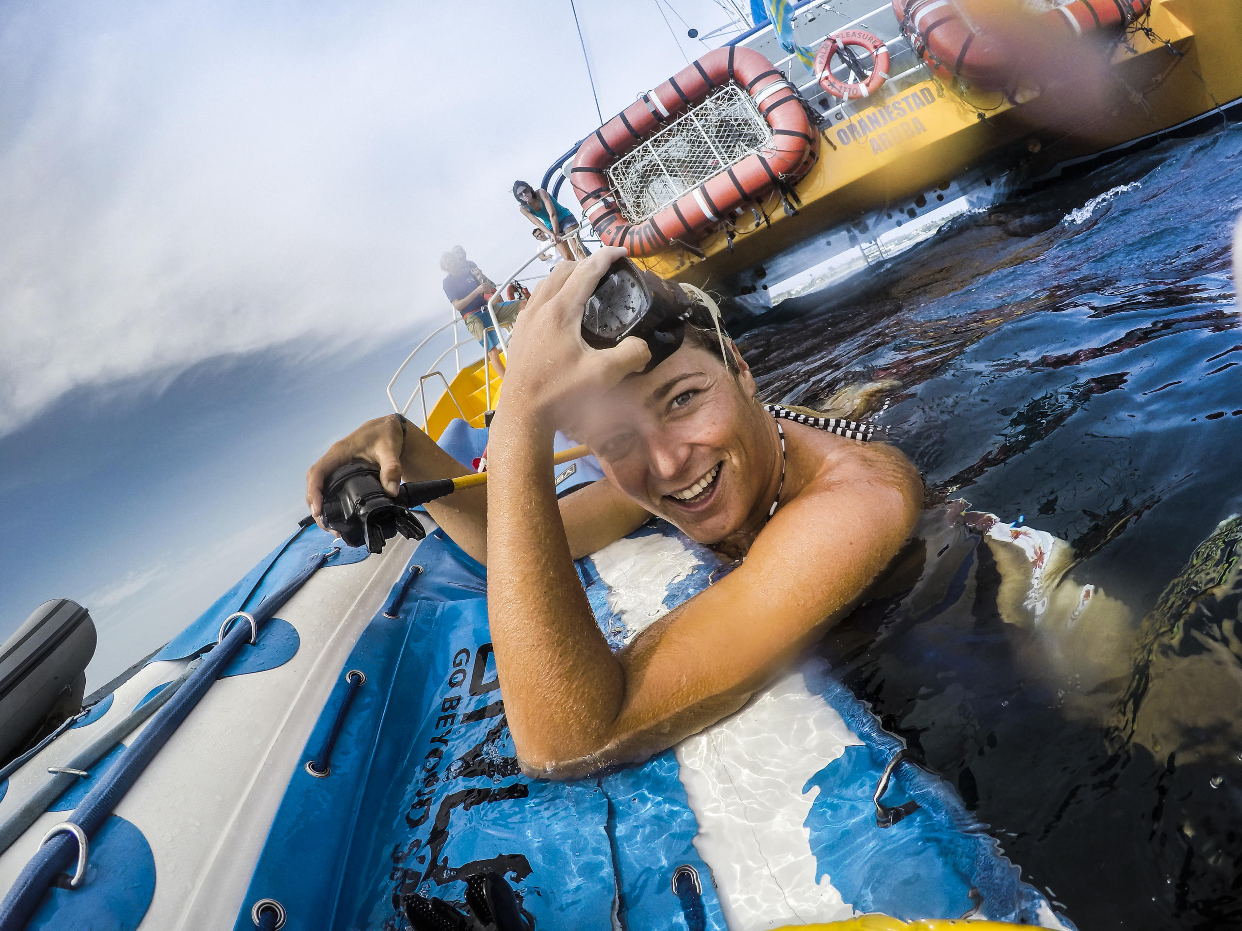 Person in water near boat, holding a snorkel, smiling at the camera.