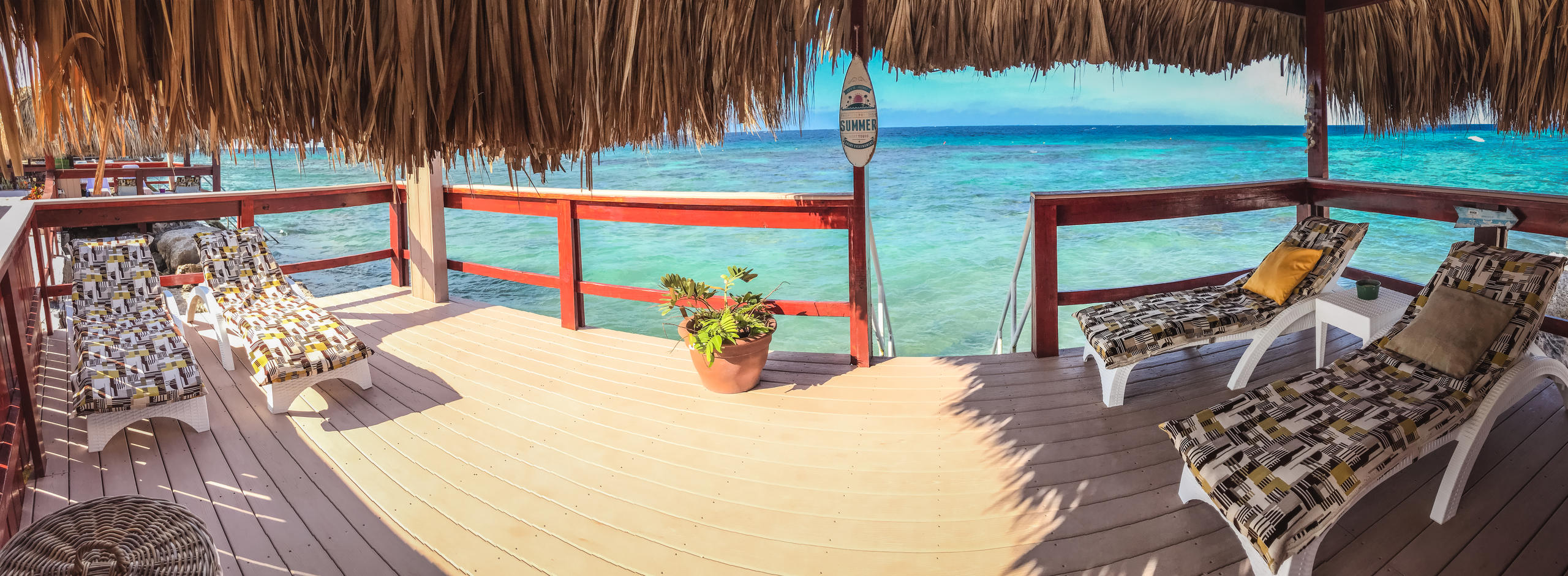 Beach hut with lounge chairs overlooking clear blue ocean.