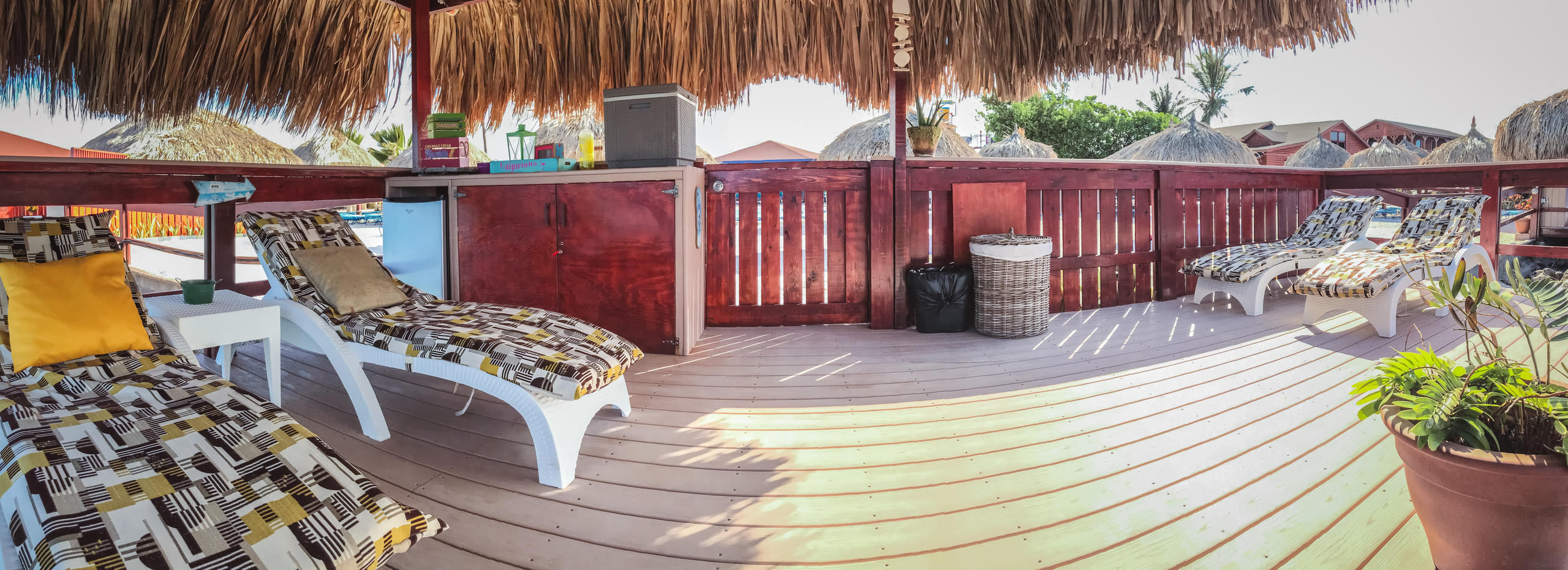 Outdoor deck with lounge chairs, thatched roof, and tropical setting.