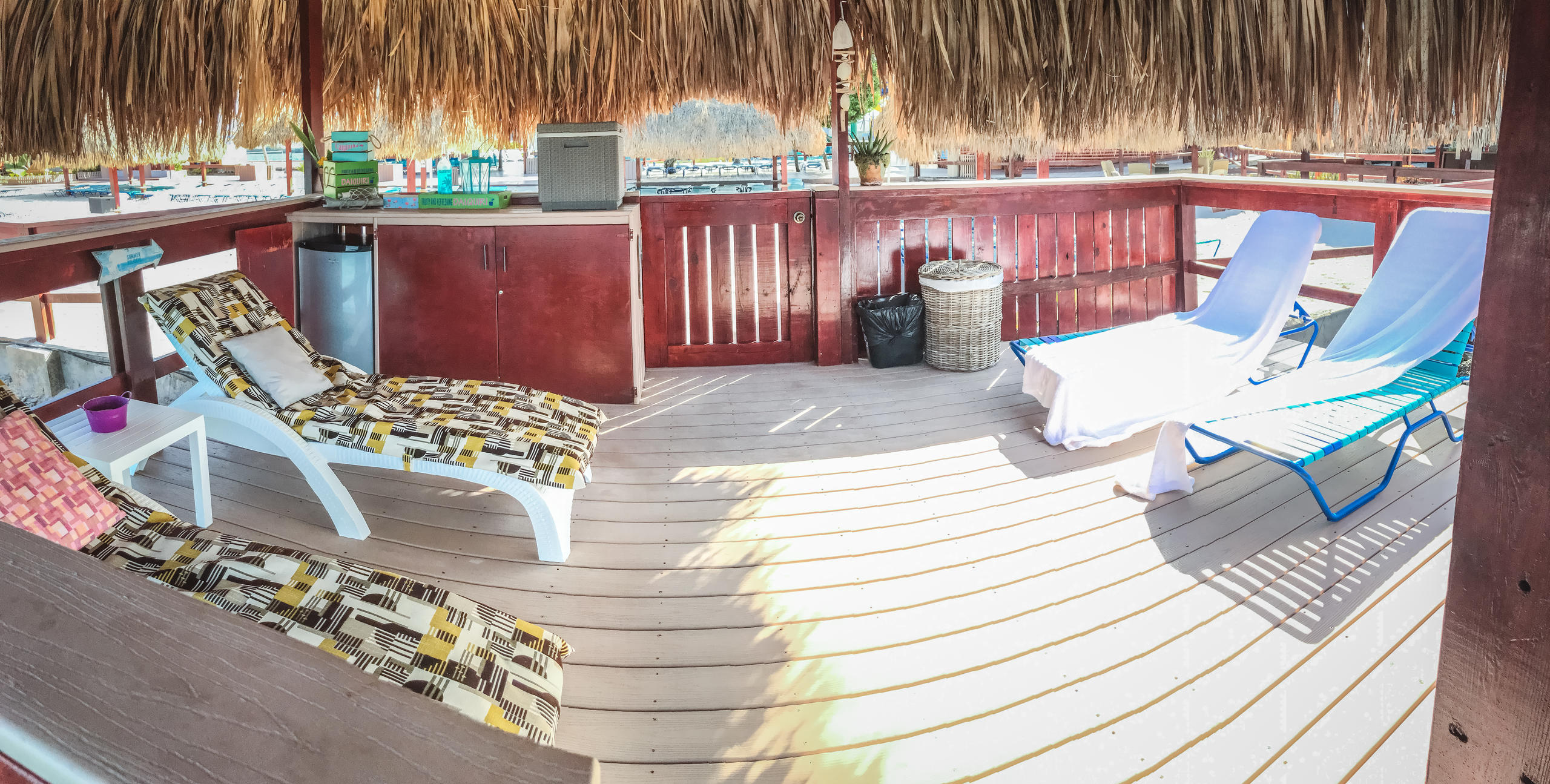 Thatched cabana with lounge chairs, mini-fridge, and a shaded wooden deck.