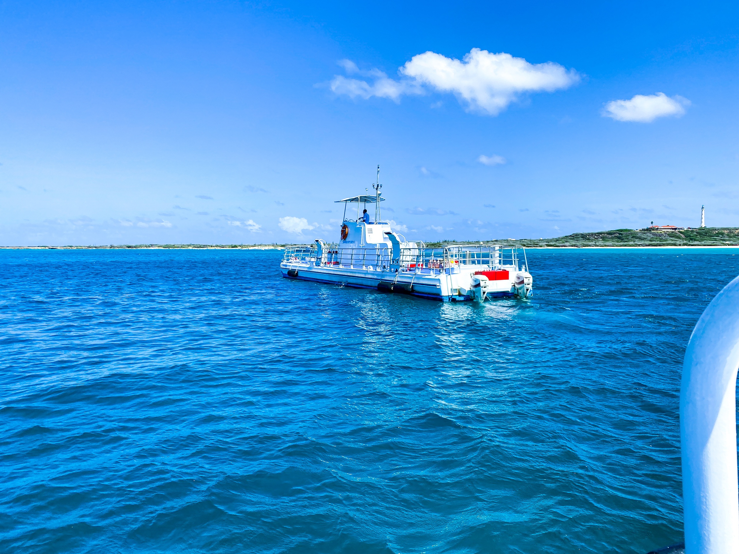 Boat on clear blue ocean under bright sky with distant shoreline.