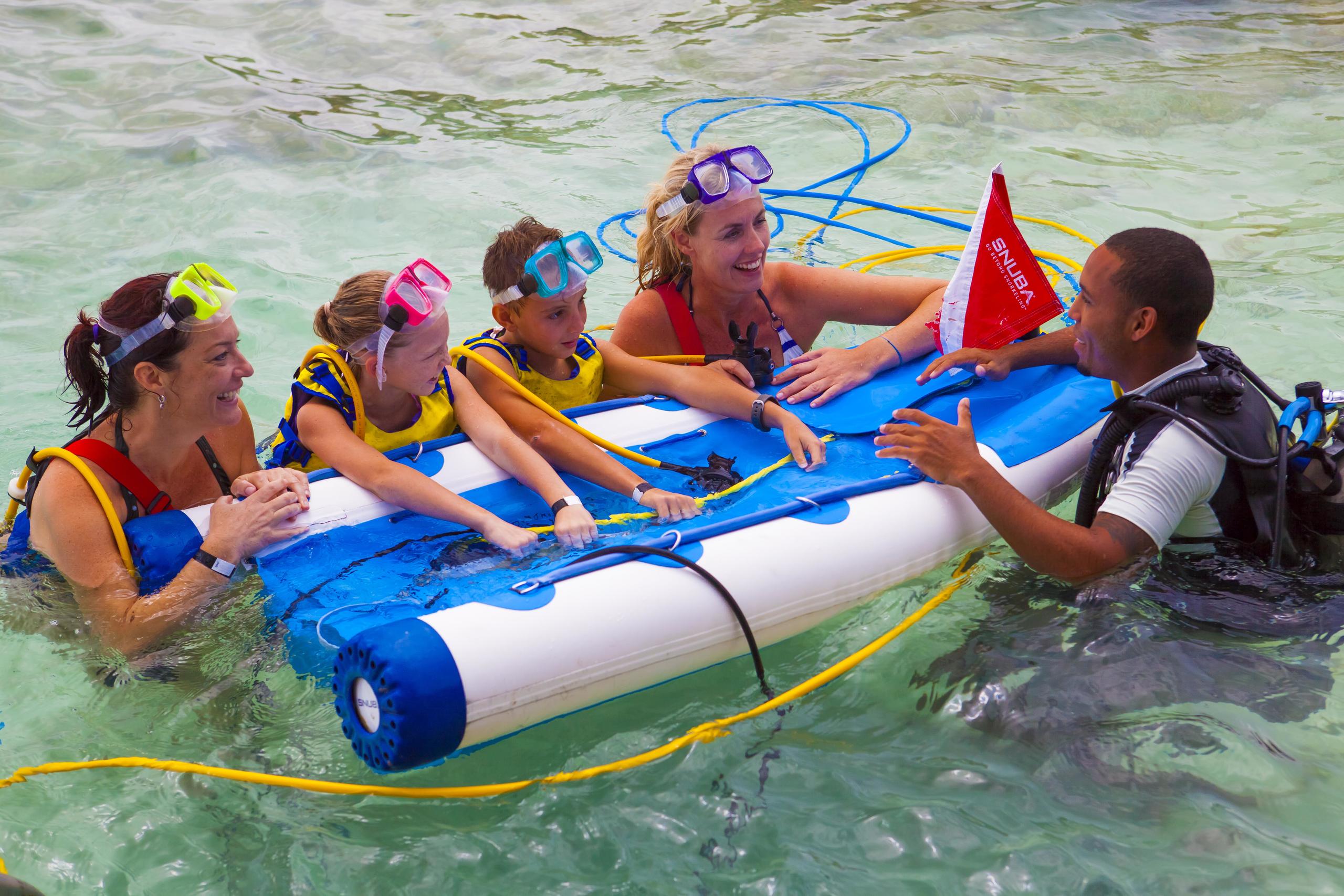 Group snorkeling lesson with inflatable raft and instructor in shallow water.
