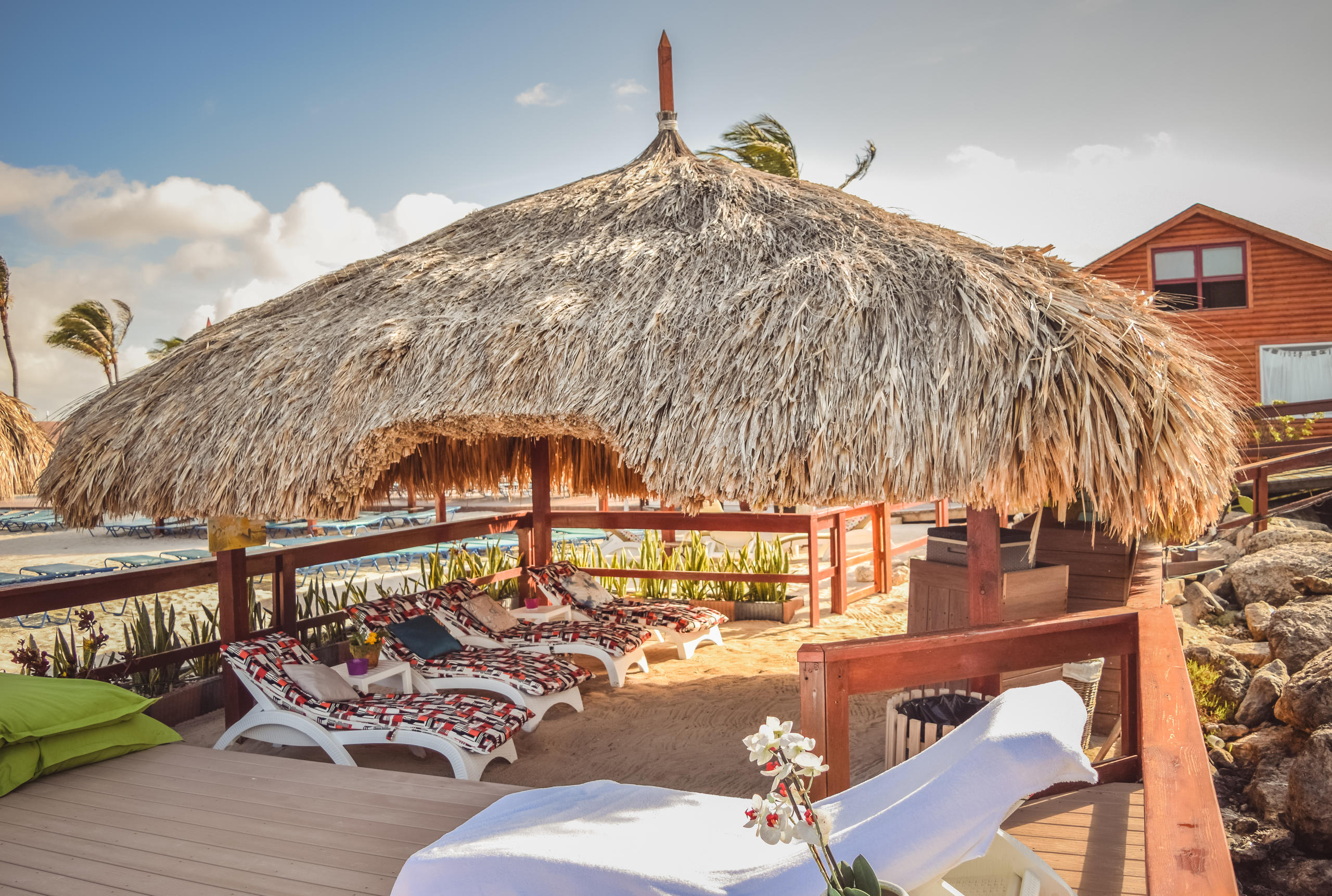 Tropical hut with loungers under a thatched roof on a sunny beach.