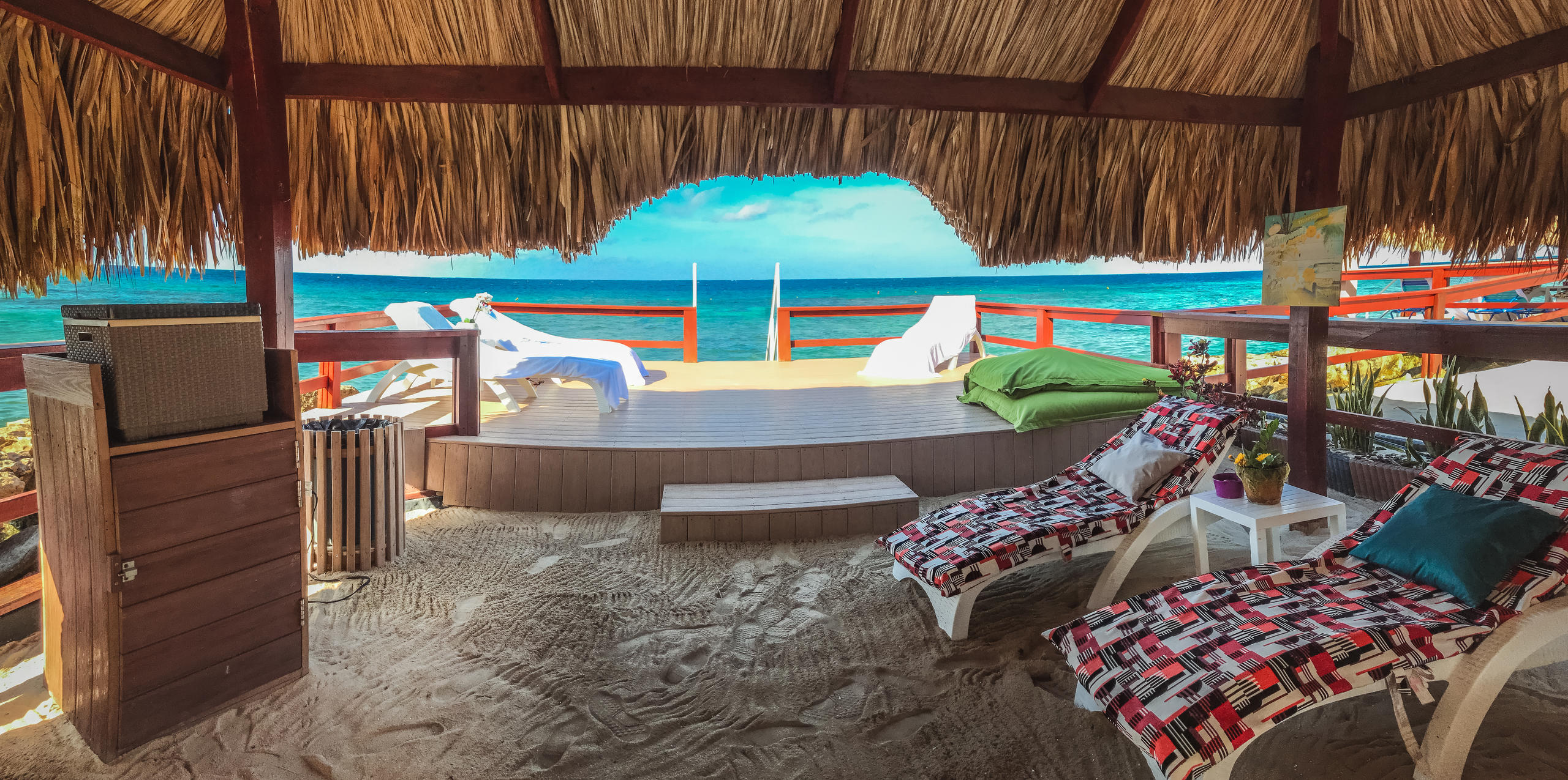 Beach cabana with loungers, straw roof, and ocean view.