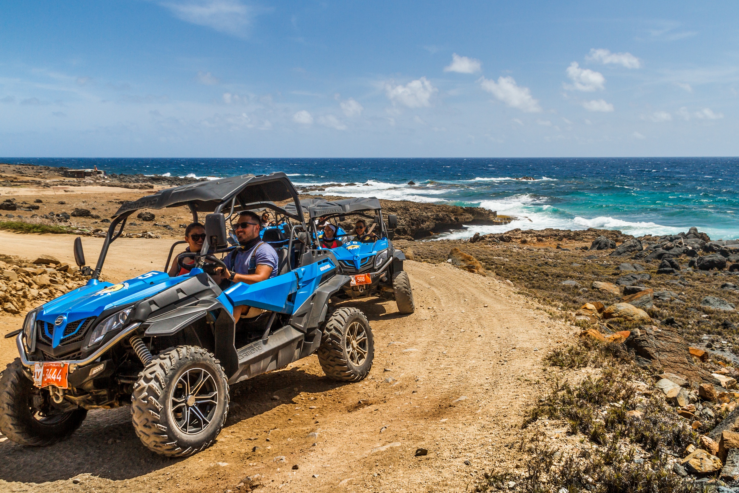 Two blue ATVs driving on rocky seaside path with ocean view.