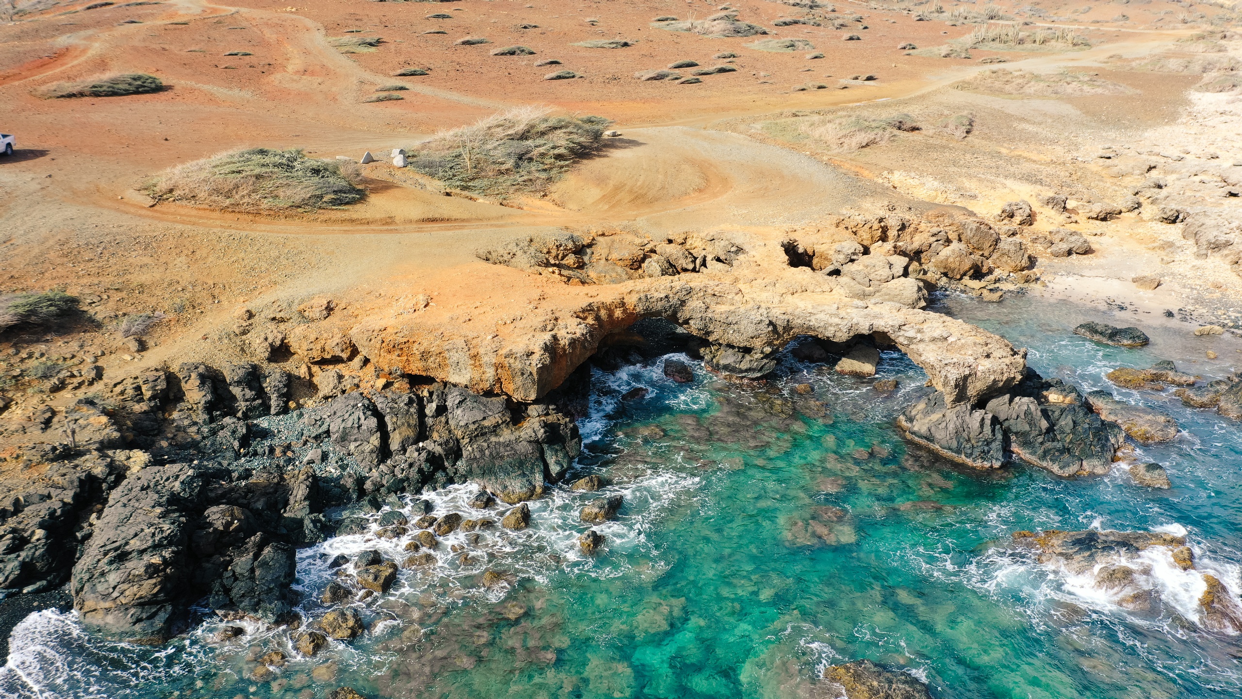 Aerial view of a rocky coastline with turquoise water and reddish-brown terrain.