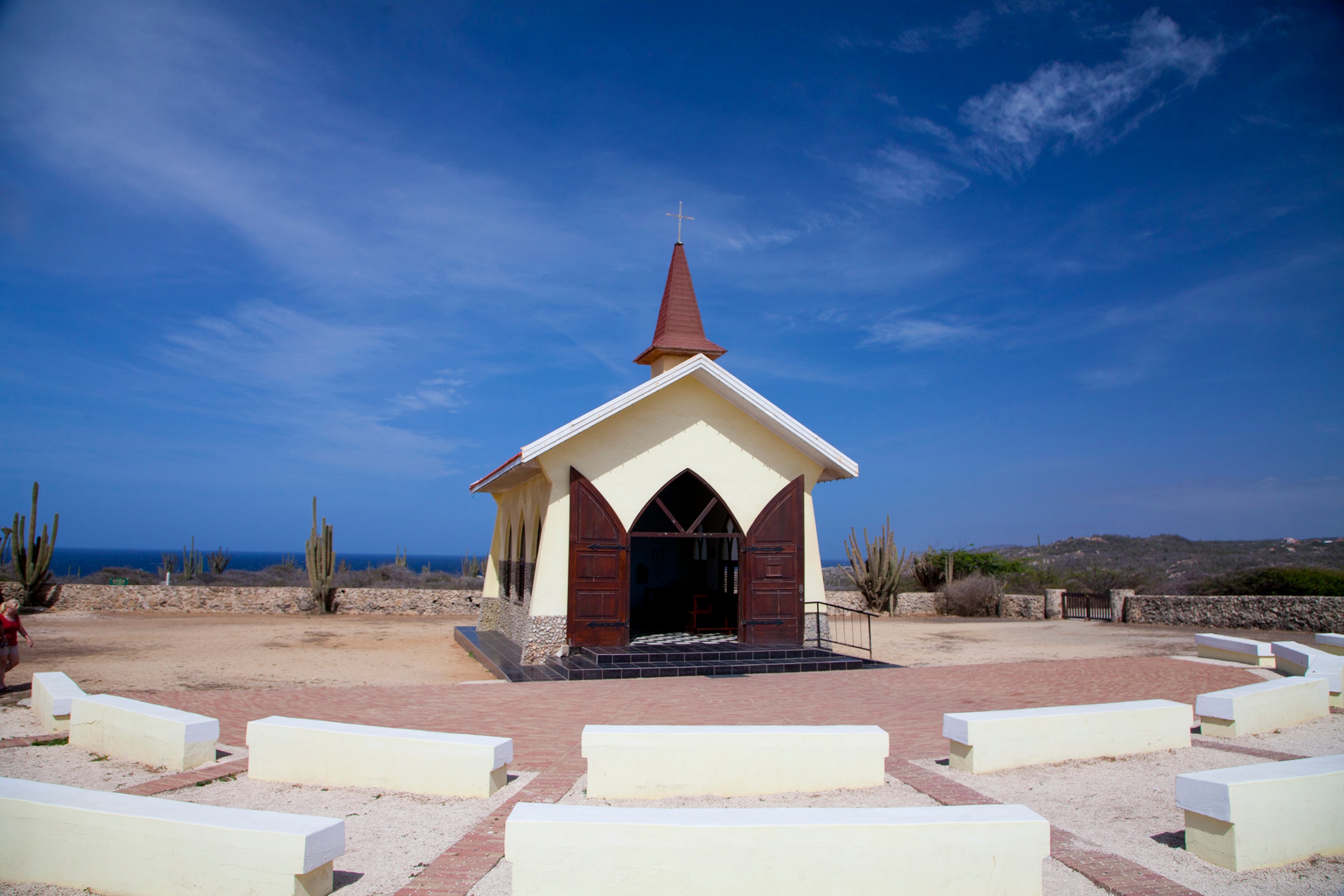 Small chapel with steeple, surrounded by benches, desert landscape, blue sky.