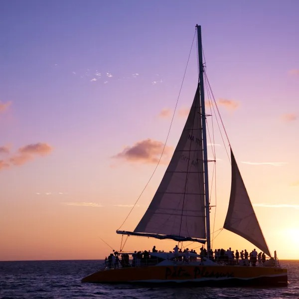 Sailboat on ocean at sunset with orange sky and clouds.
