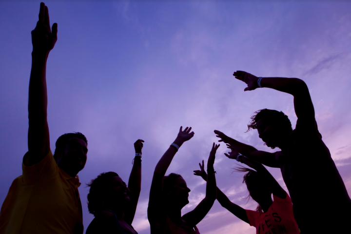 Silhouettes of people dancing against a purple sunset sky.