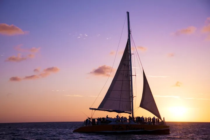 Silhouetted sailboat at sunset with pink sky.