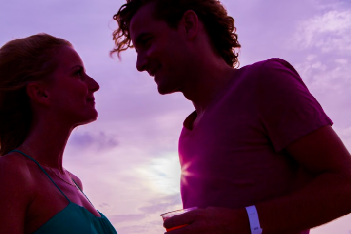 Silhouetted couple gazing at each other against a purple sunset sky.