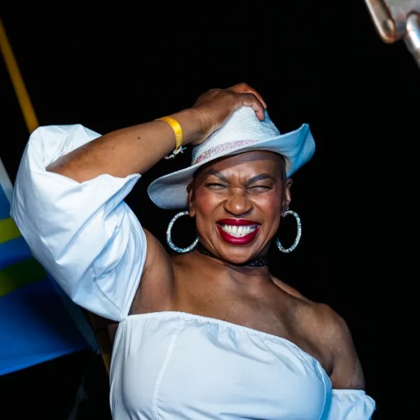 Woman smiling, wearing white hat and top, festive background.