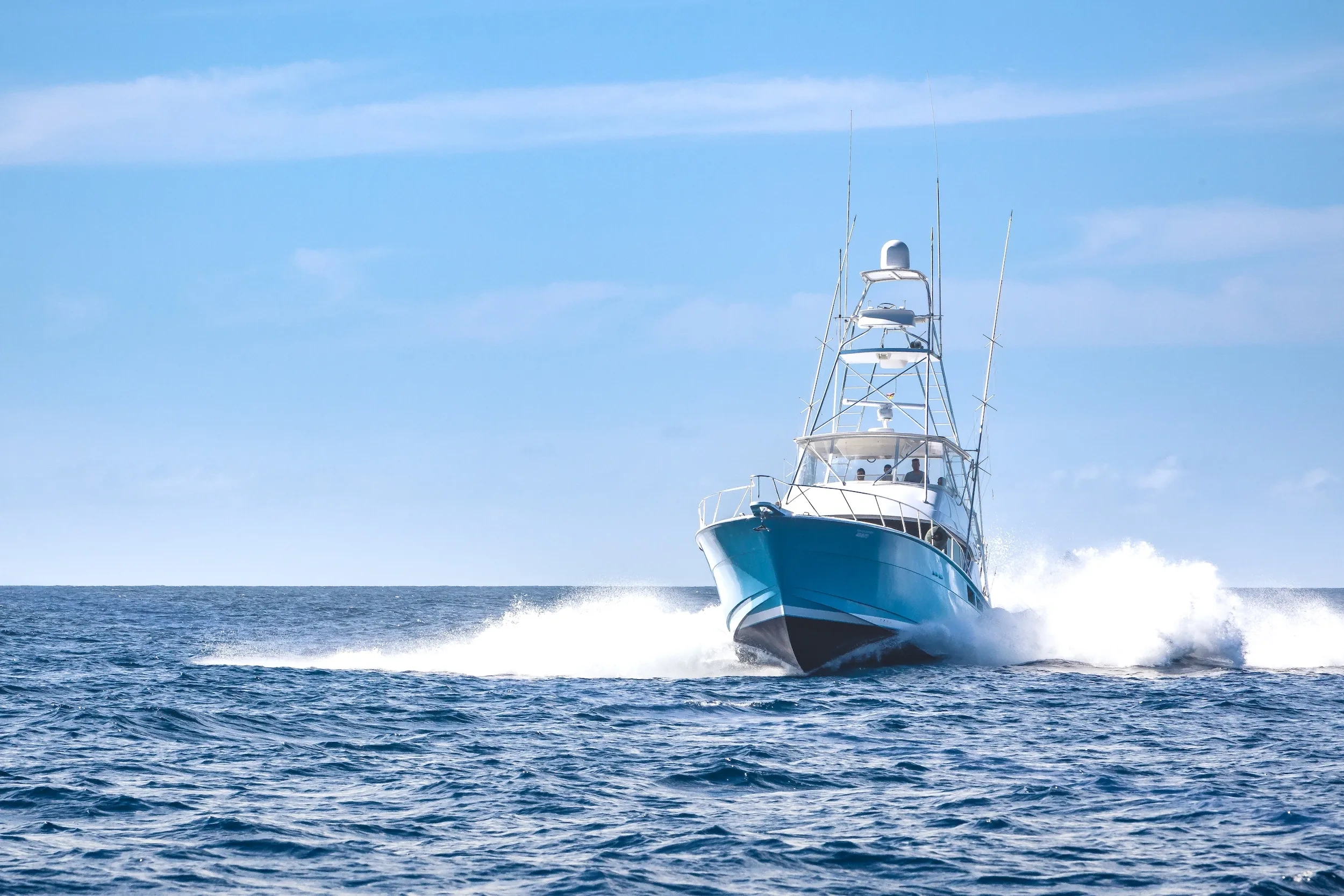 Boat speeding on the ocean with white waves under a clear blue sky.