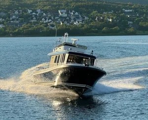 Boat speeding on water with town and trees in background.
