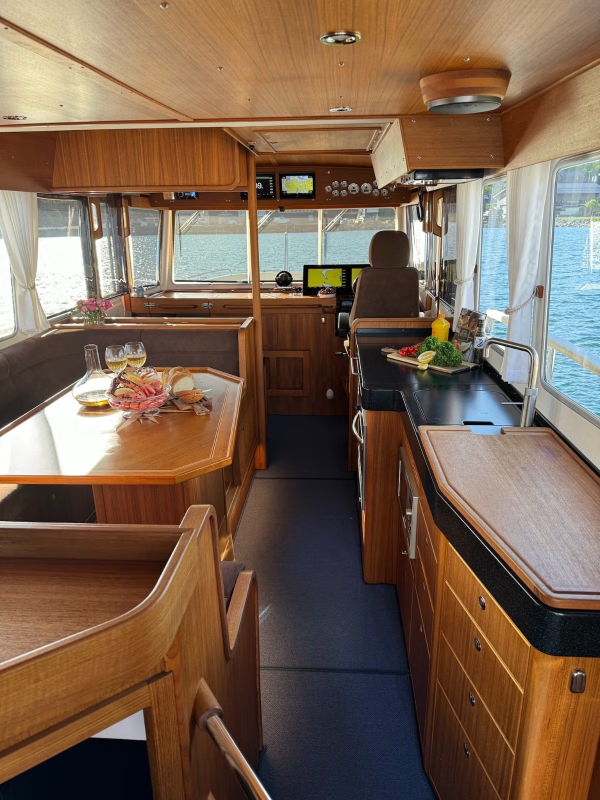 Boat interior with wood paneling, dining area, and steering wheel.