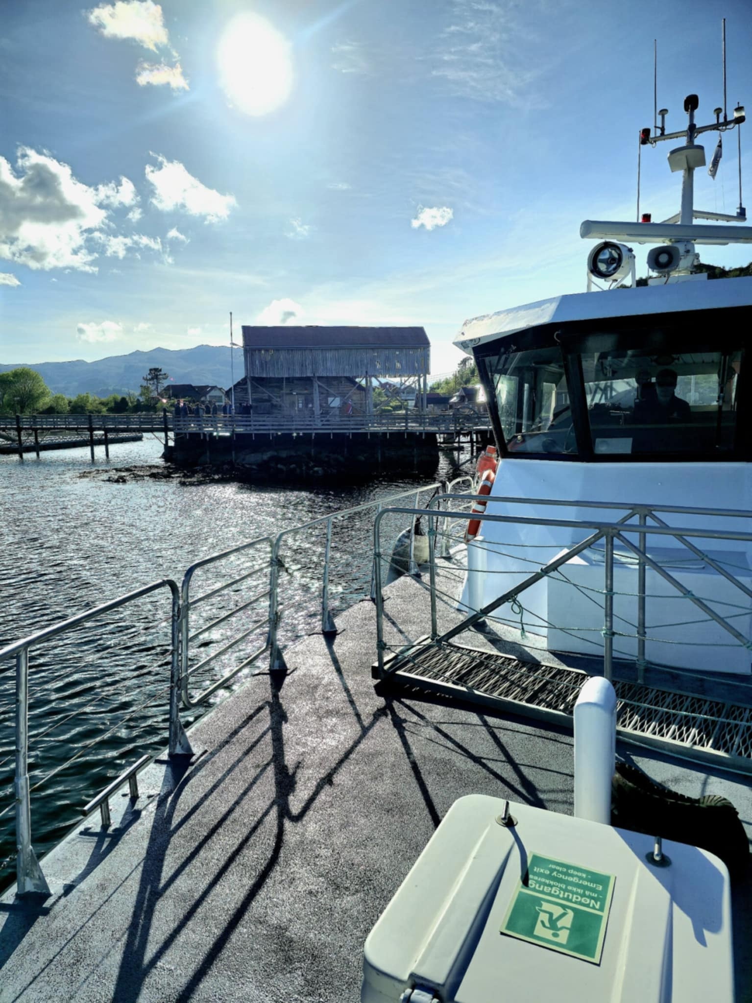 Boat docked at a pier under a sunny sky with a building in the background.