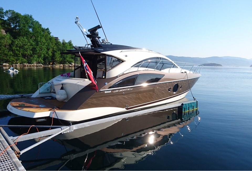 Luxury yacht docked on calm water with forested shoreline in background.