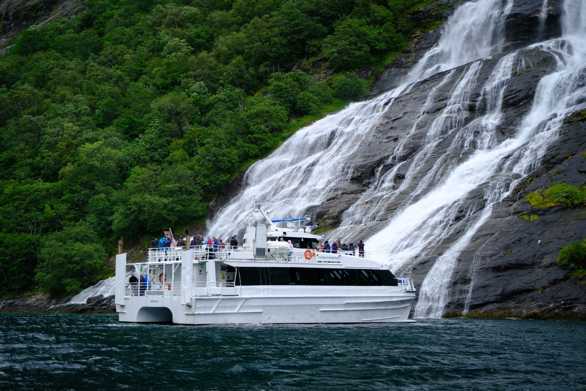 Boat cruising near a waterfall with lush green surroundings.