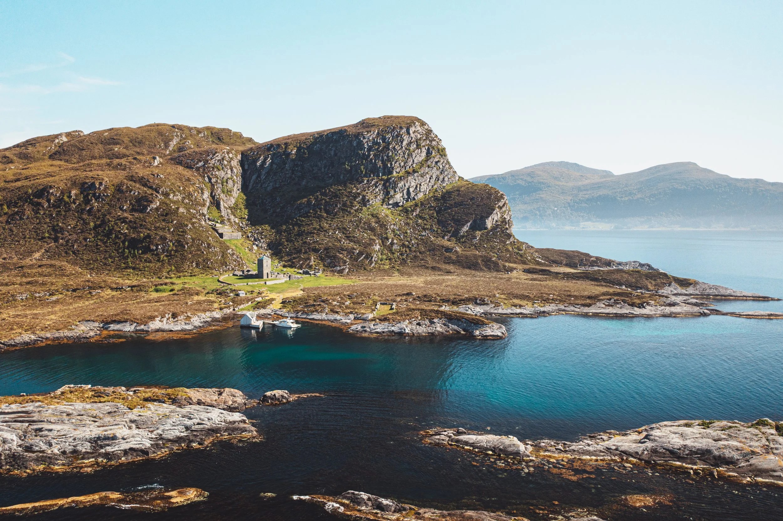 Coastal landscape with cliffs, a small building, and calm blue water.