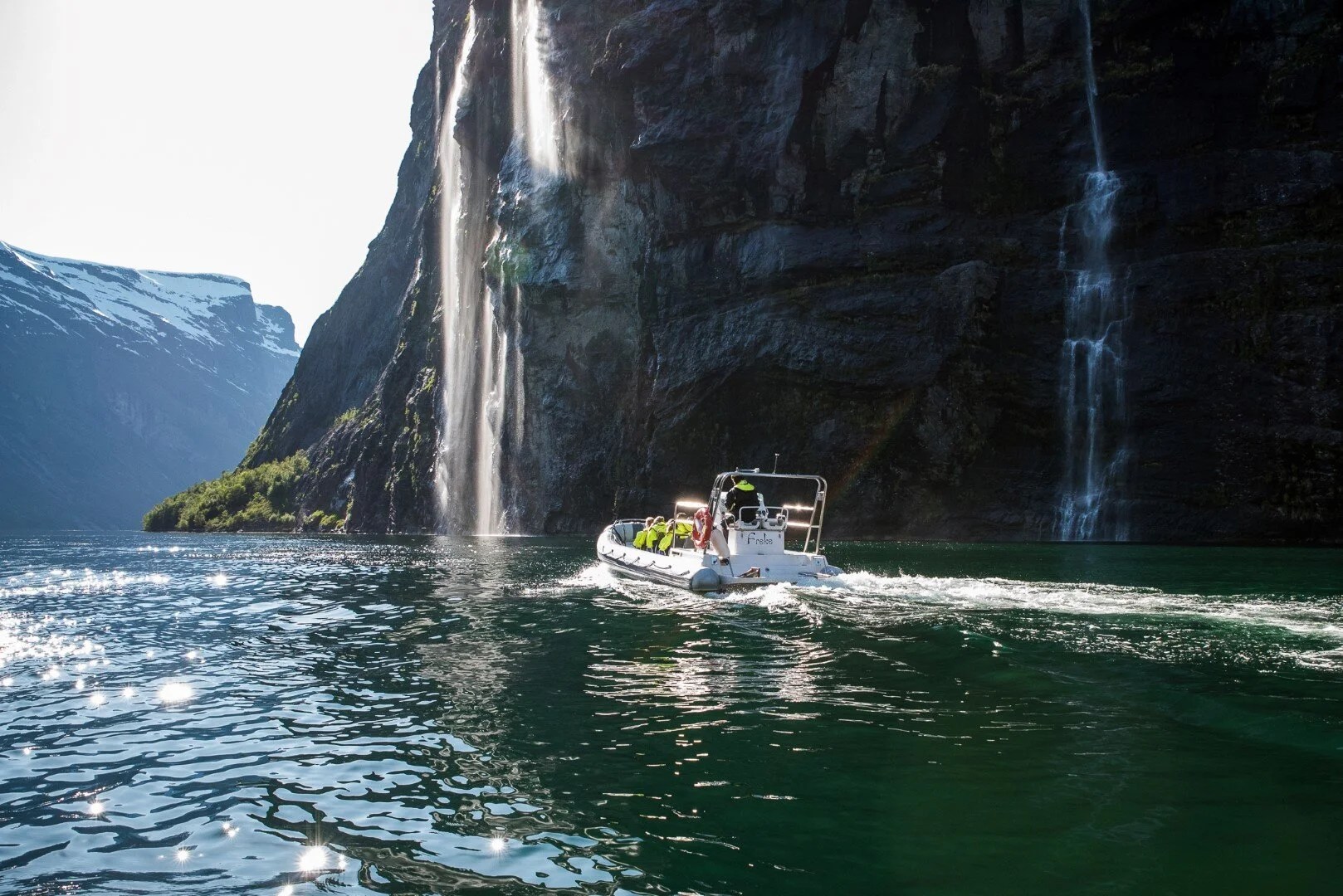 Boat on a fjord with waterfalls cascading down rocky cliffs.