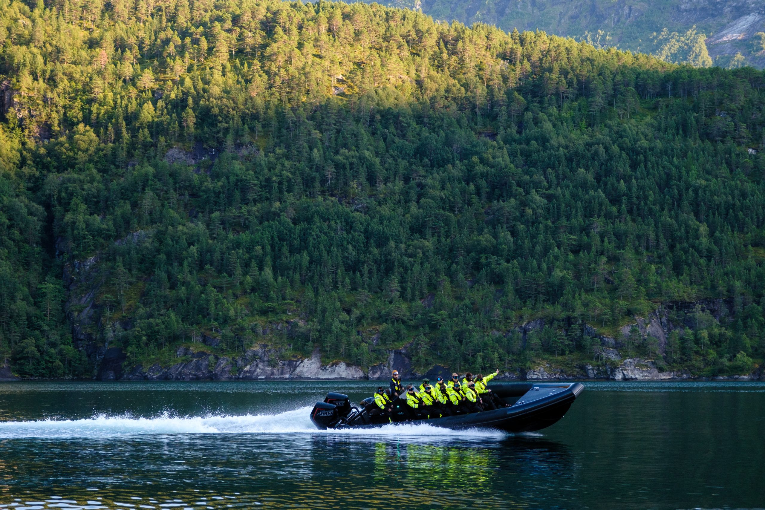 People in yellow jackets on a speedboat in front of a forested hillside.