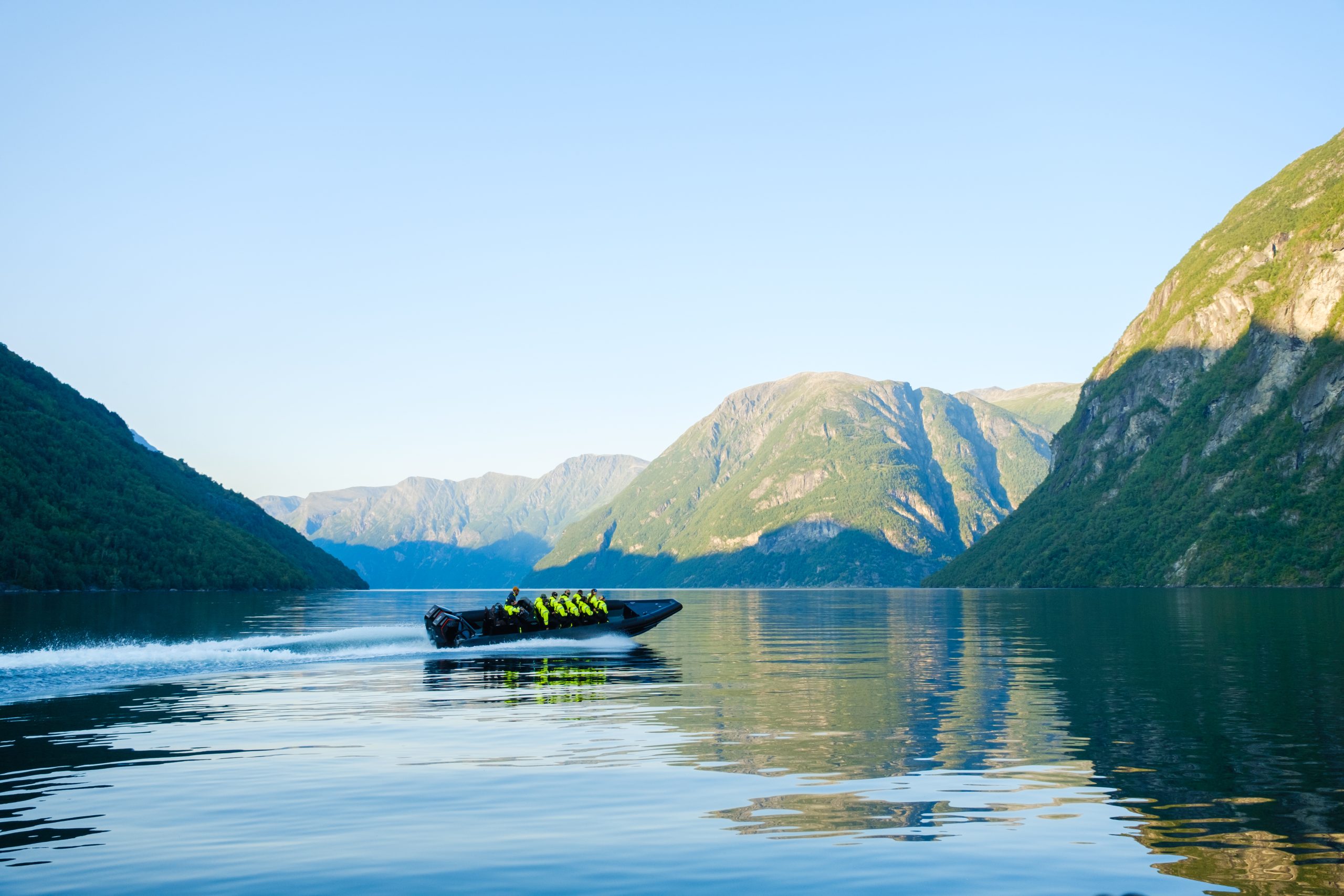 Motorboat with passengers in life jackets on a calm fjord surrounded by mountains.