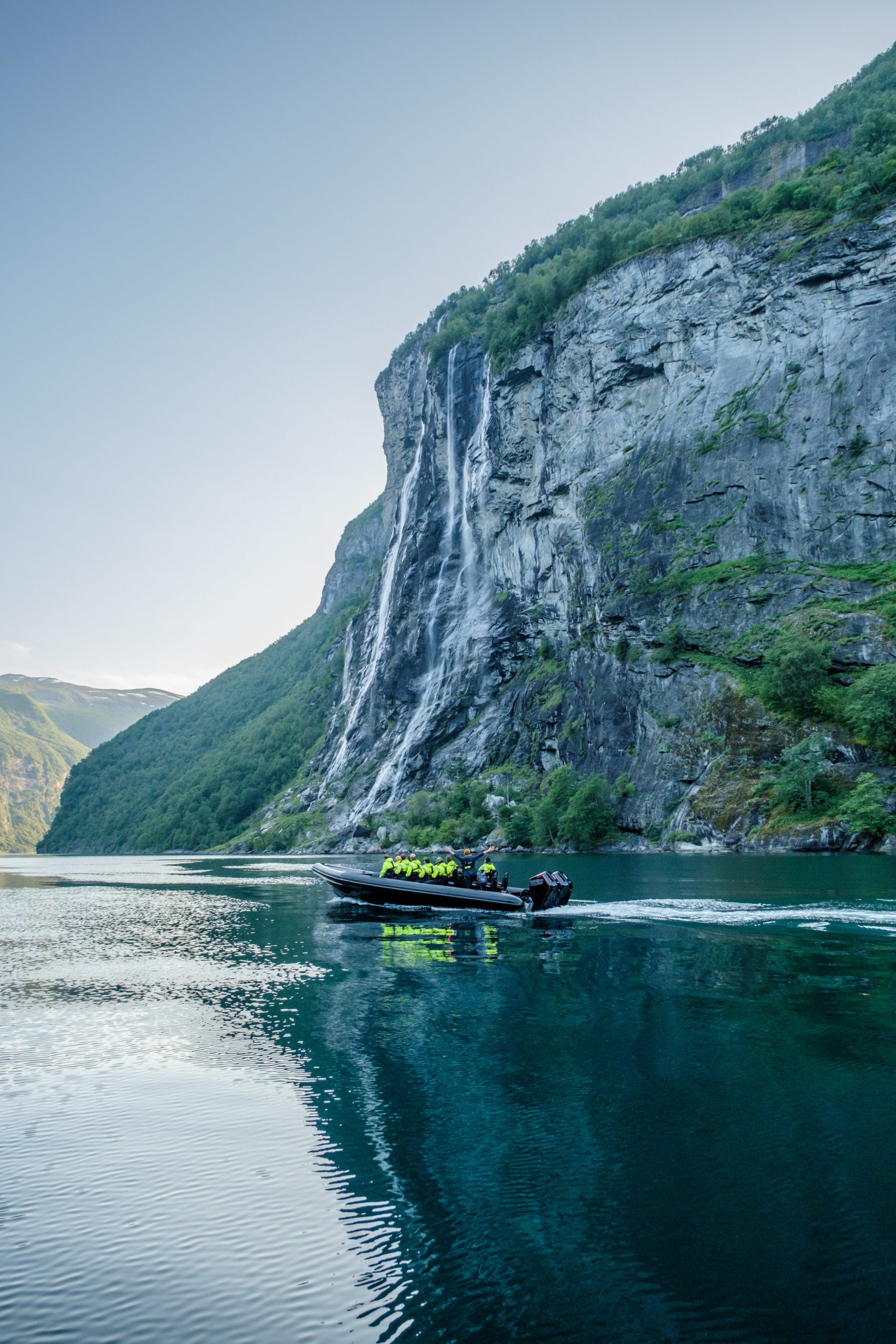 Boat on a calm fjord with a waterfall cascading down a steep, rocky cliff.