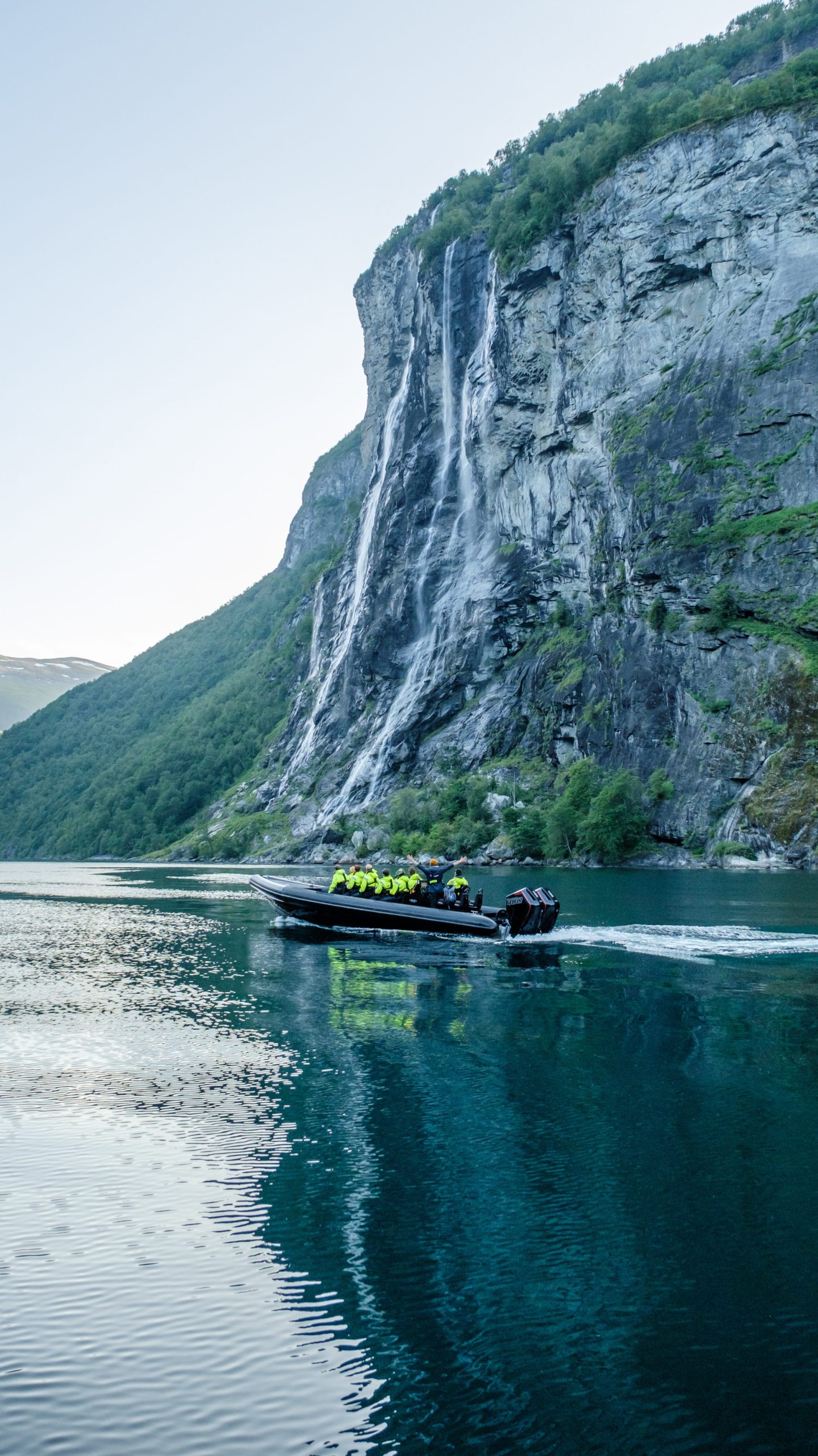 A boat with passengers on a lake near a waterfall and steep cliff.
