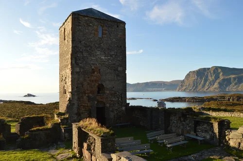Ancient stone tower and ruins by a coastal landscape under clear sky.