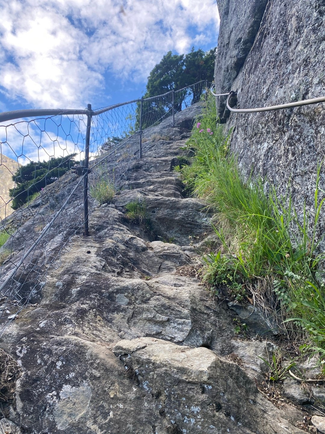 Rocky mountain path with railing and clouds above.