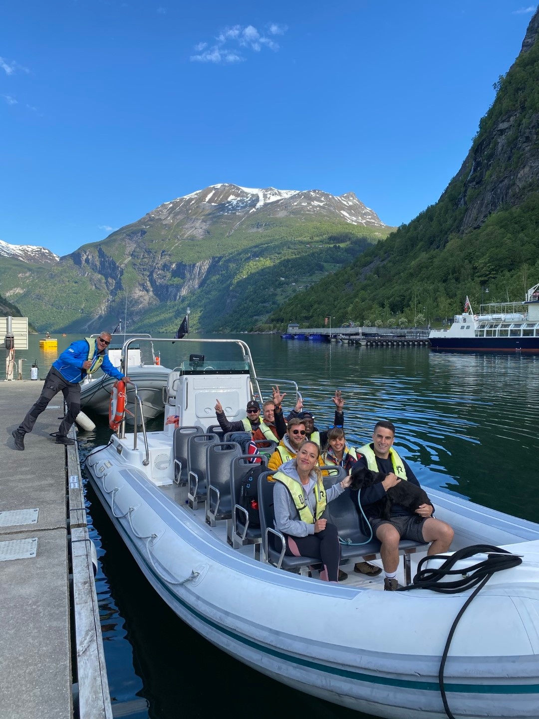 People on a boat near a dock with mountains and a clear blue sky.