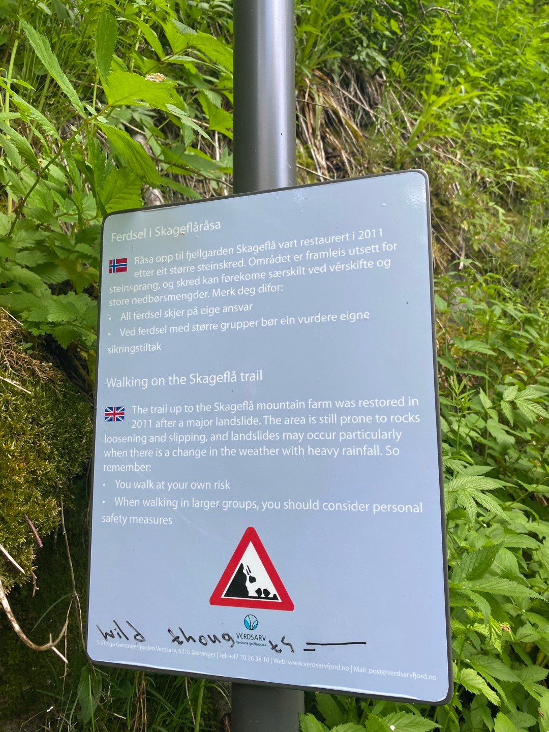 Bilingual trail sign in nature with greenery around.