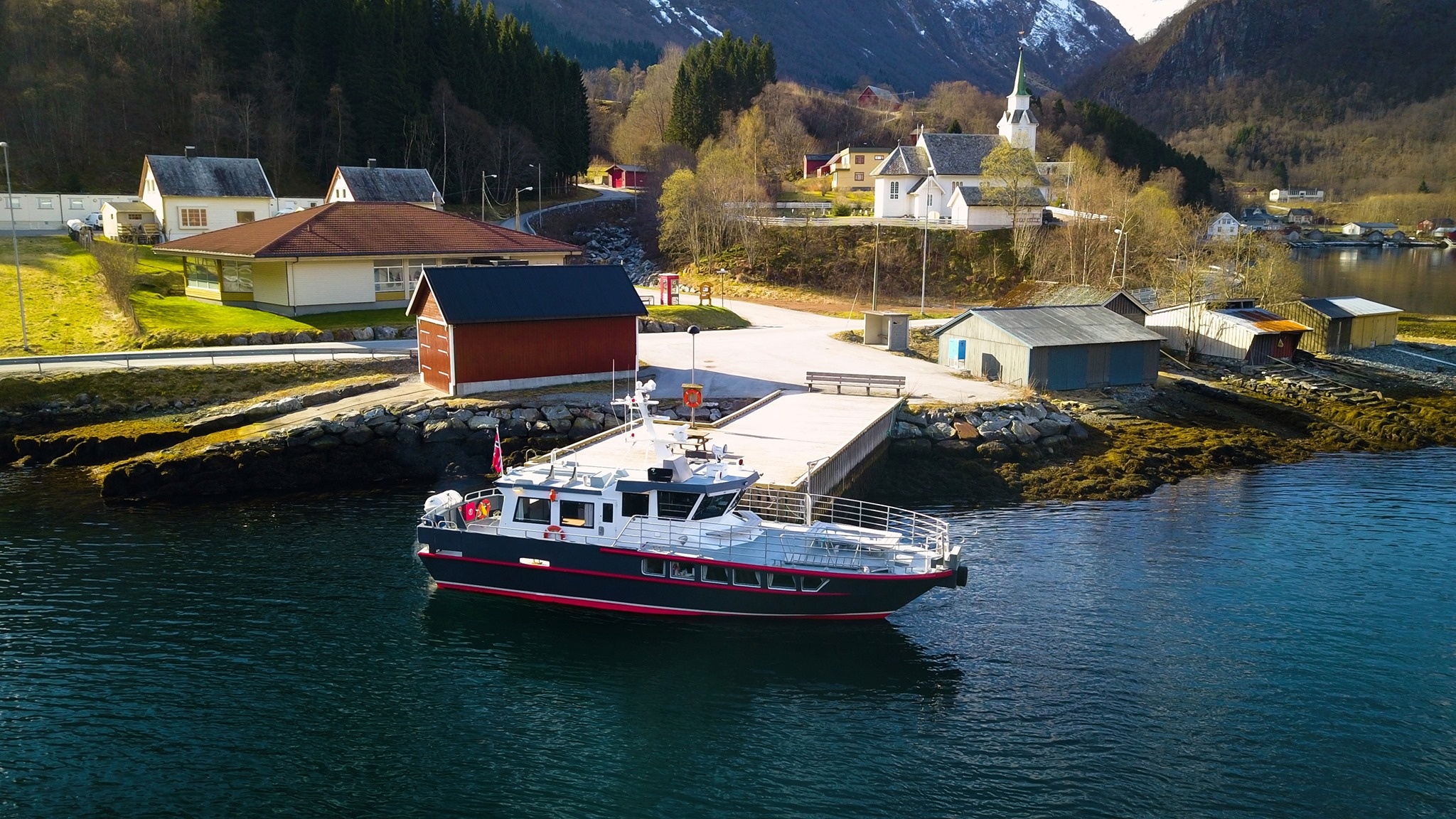 Boat on calm water near a small coastal village with mountains in the background.