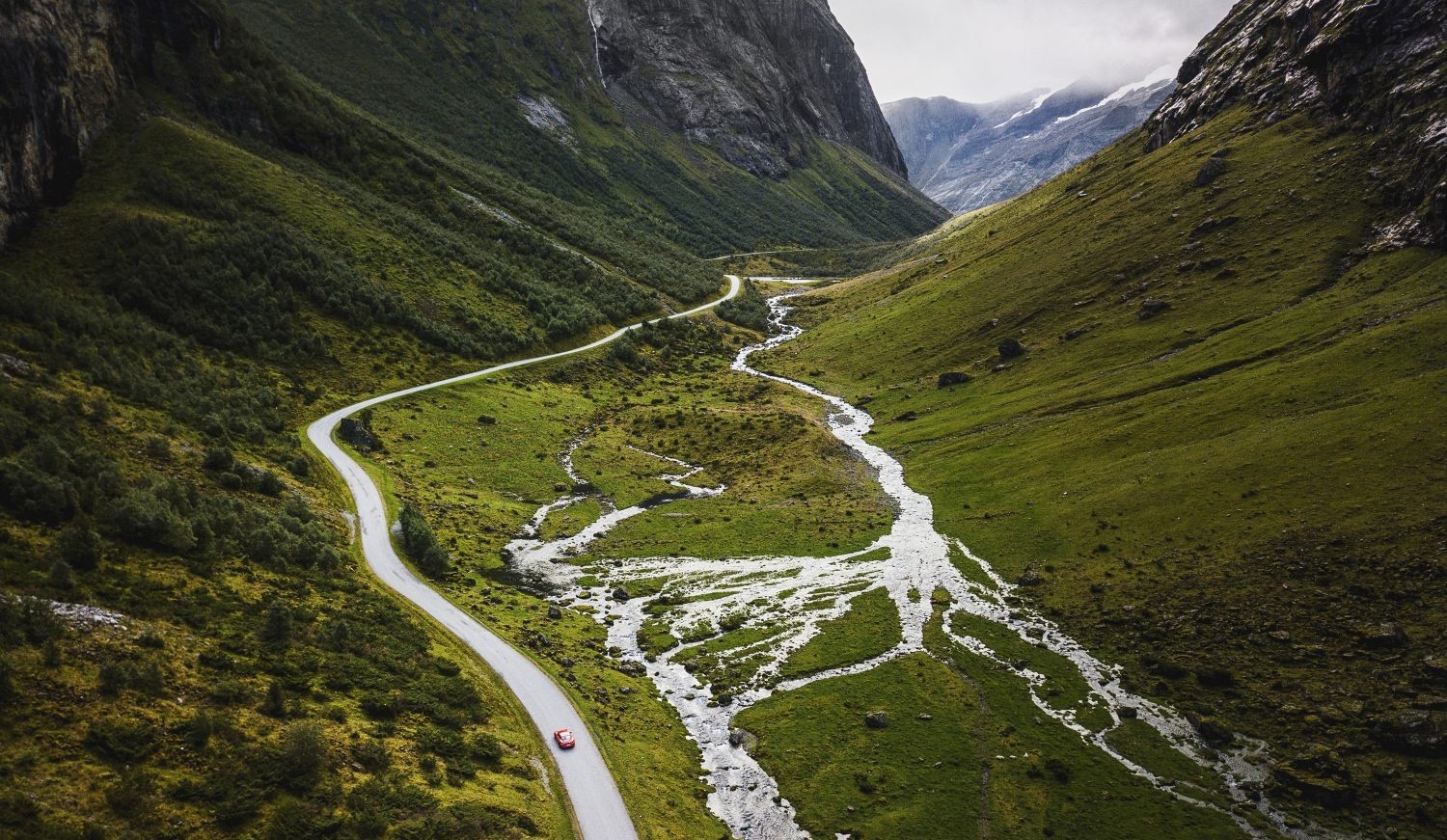 Aerial view of a winding road through a lush green valley with a river flowing beside it.