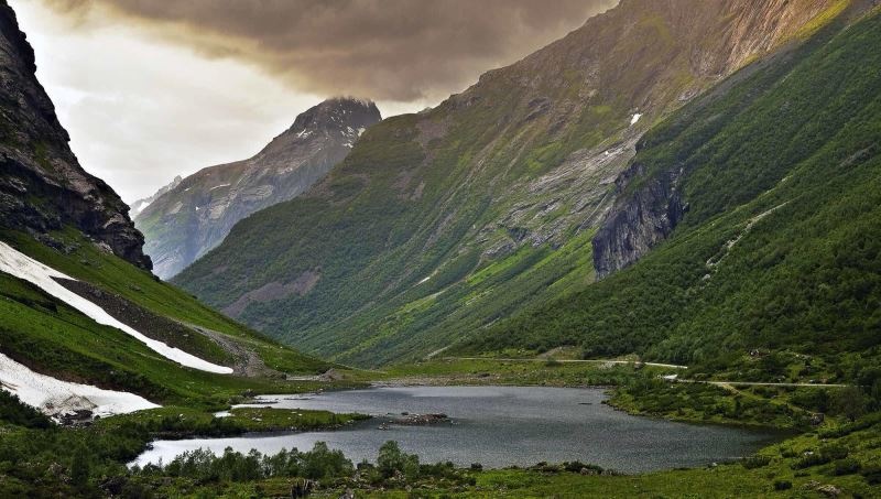 A serene mountain valley with a lake and green slopes under a cloudy sky.