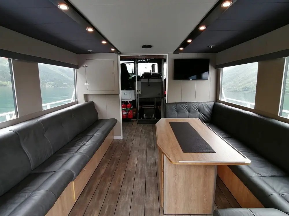 Interior of a modern boat cabin with long sofas and a wooden table.