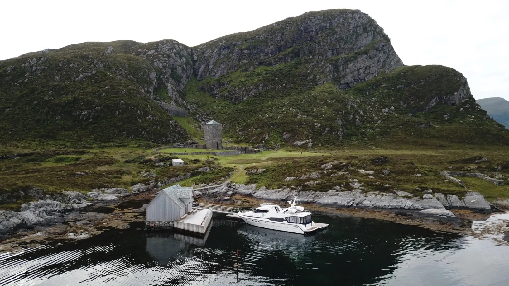 Boat docked at a small pier near rugged hills and a rocky shoreline.