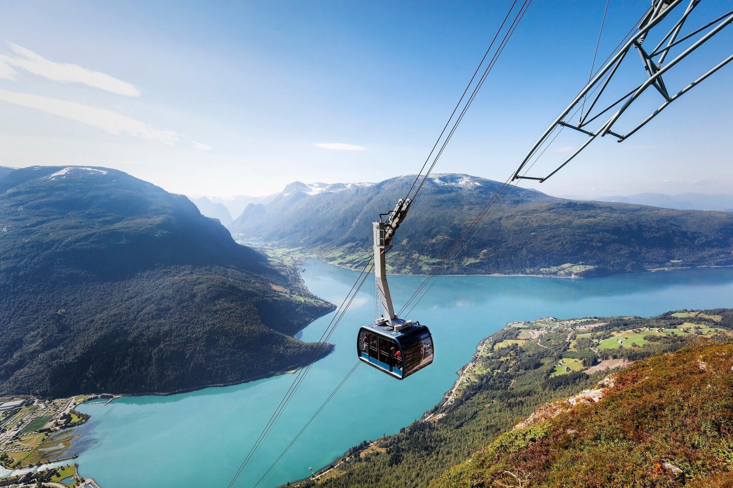 Cable car over turquoise lake and mountains under a blue sky.