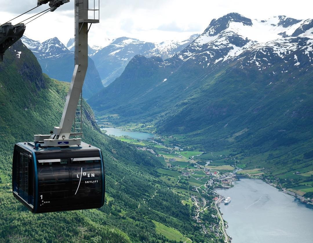 Cable car overlooking a scenic valley with mountains and a fjord.