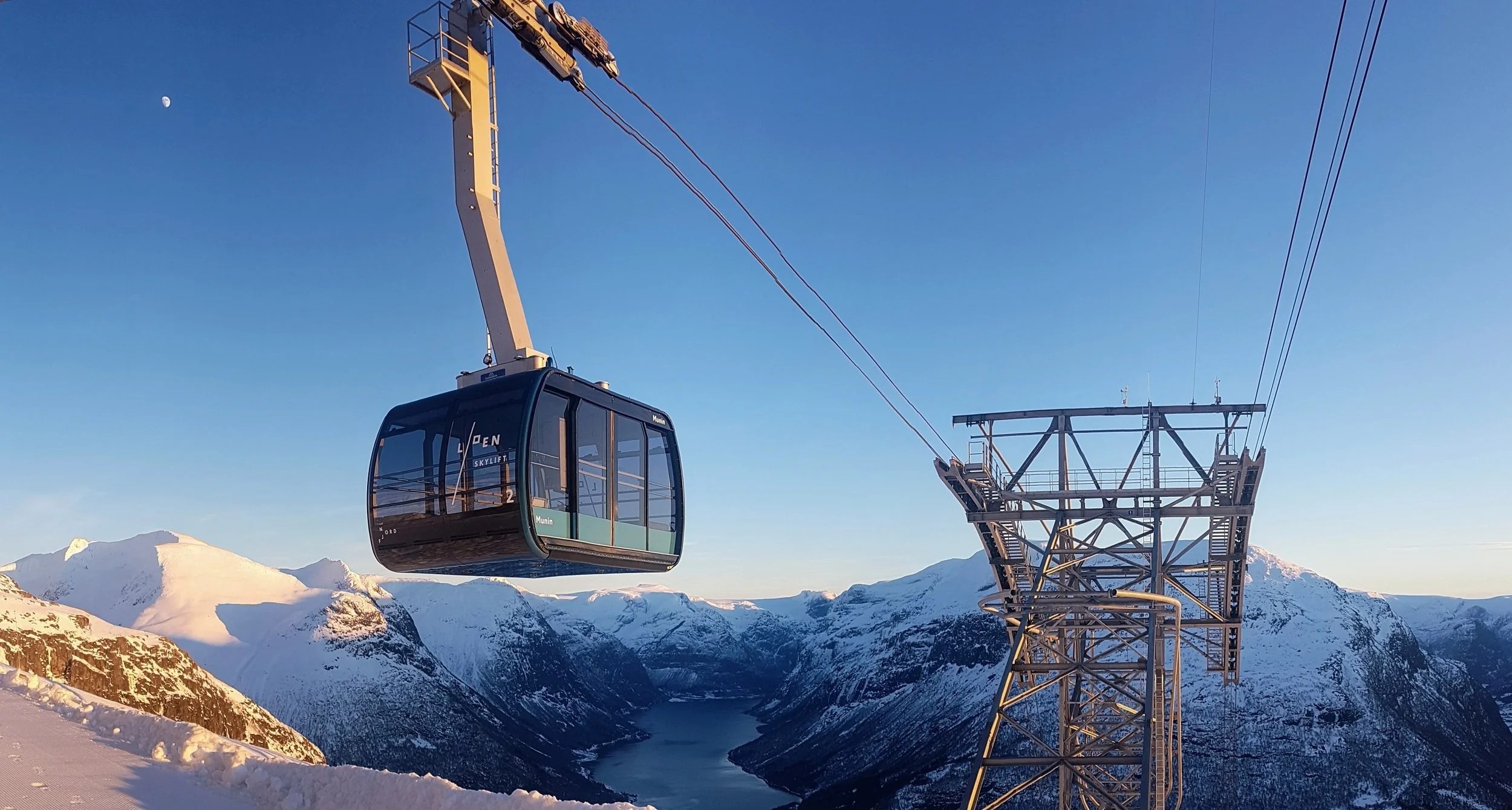 Cable car suspended over snowy mountains at sunset.