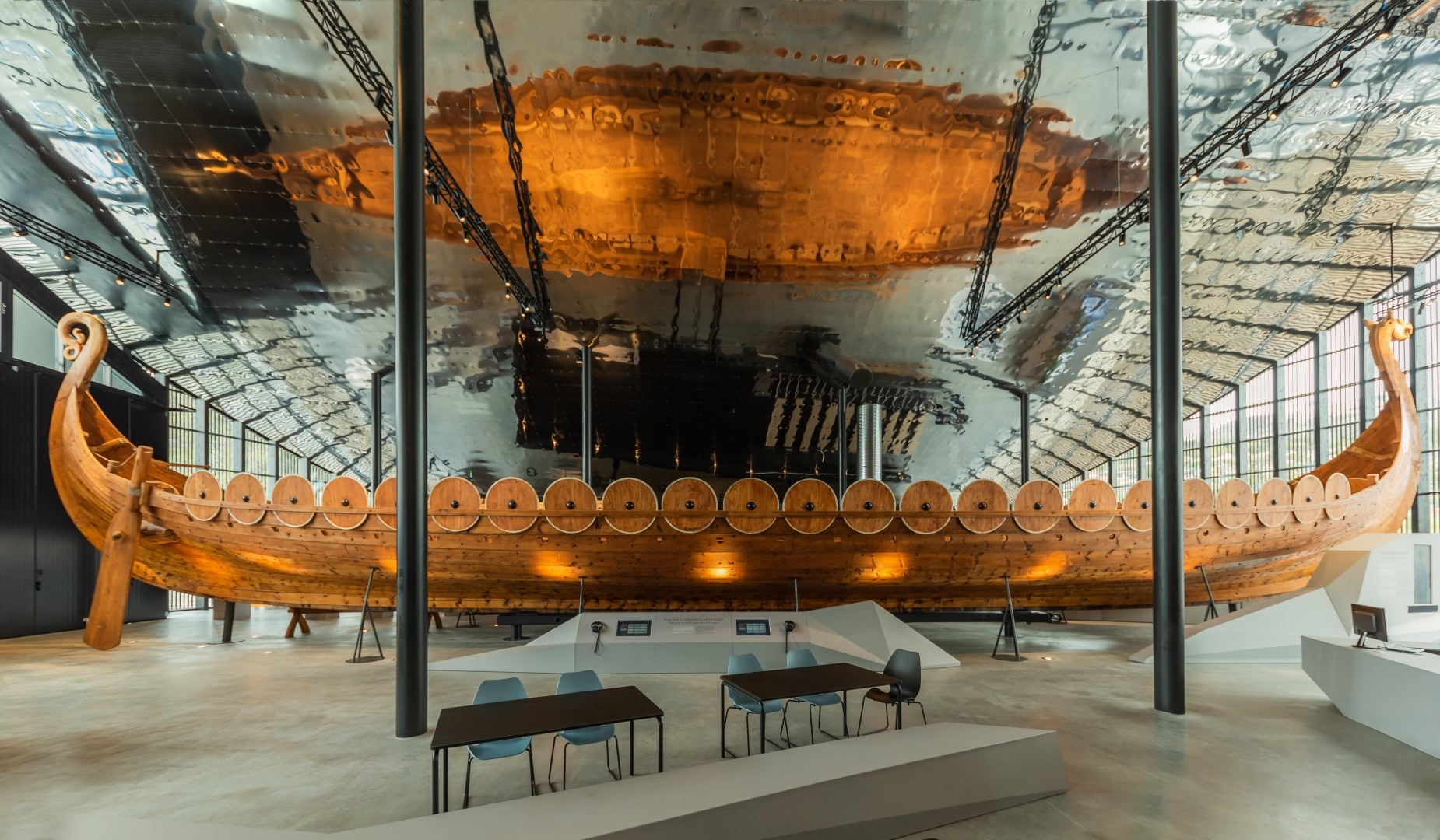 Large wooden Viking ship displayed in a modern museum setting with reflective ceiling.