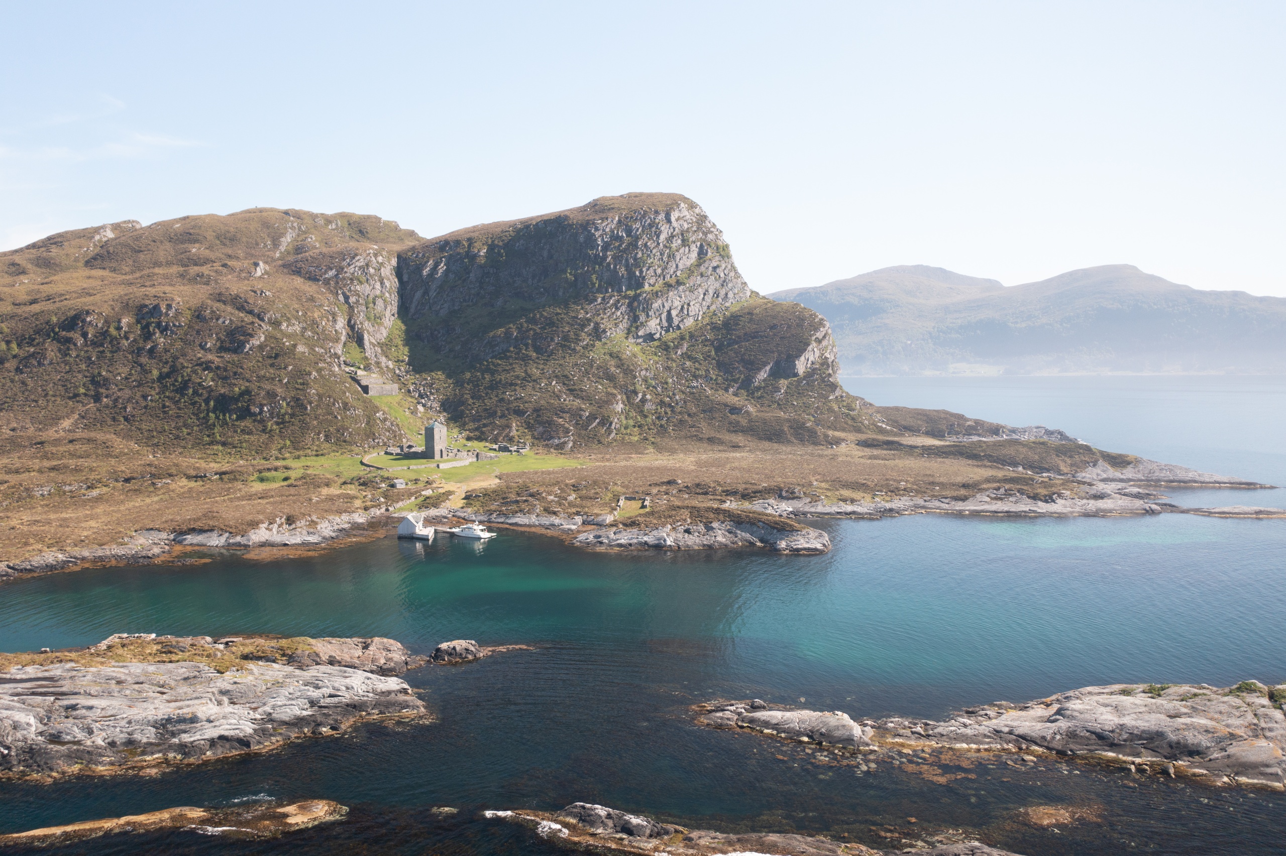 Coastal landscape with cliffs, a small building, and calm blue water under a clear sky.