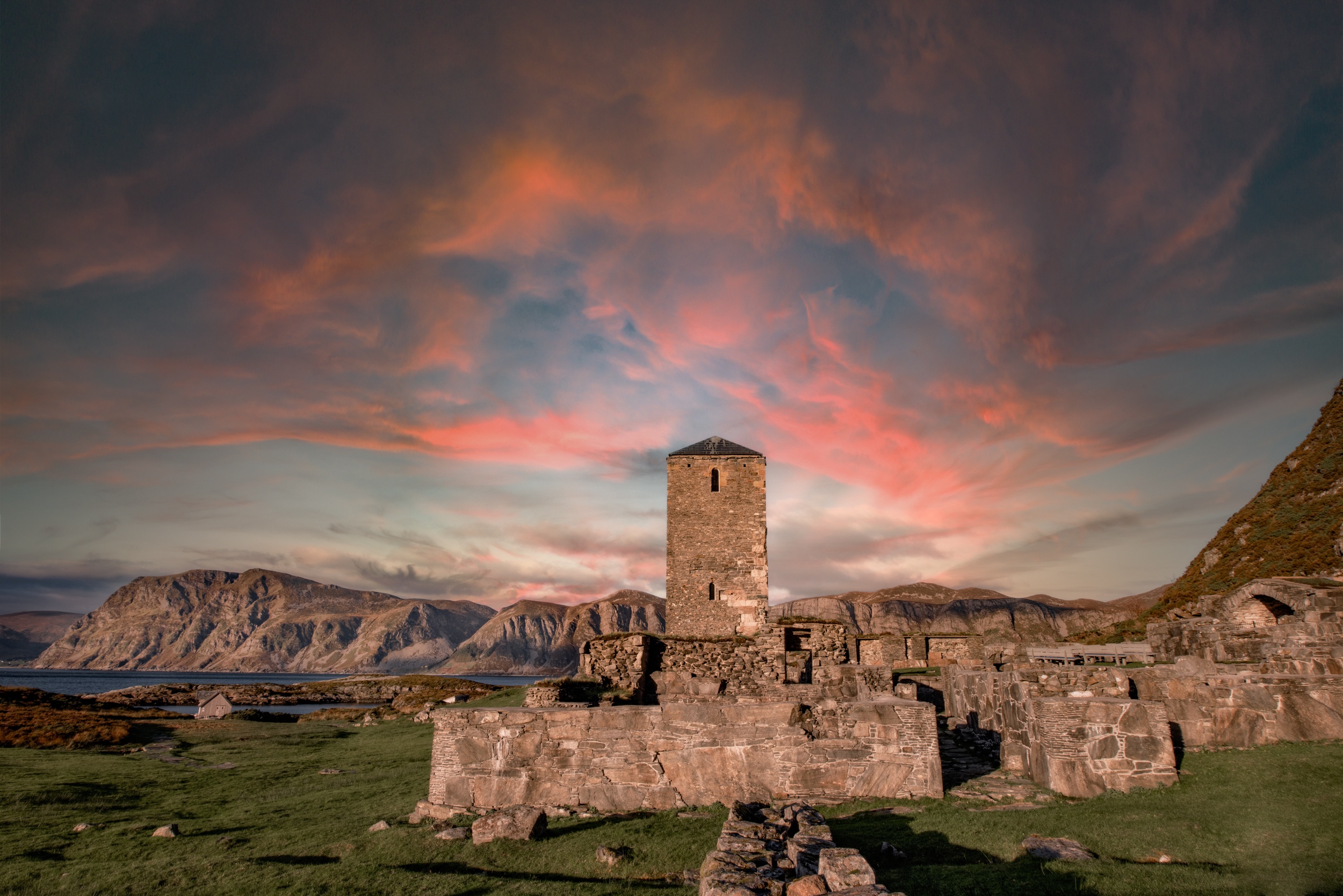 Stone ruins with tower against dramatic pink and orange sky at sunset.