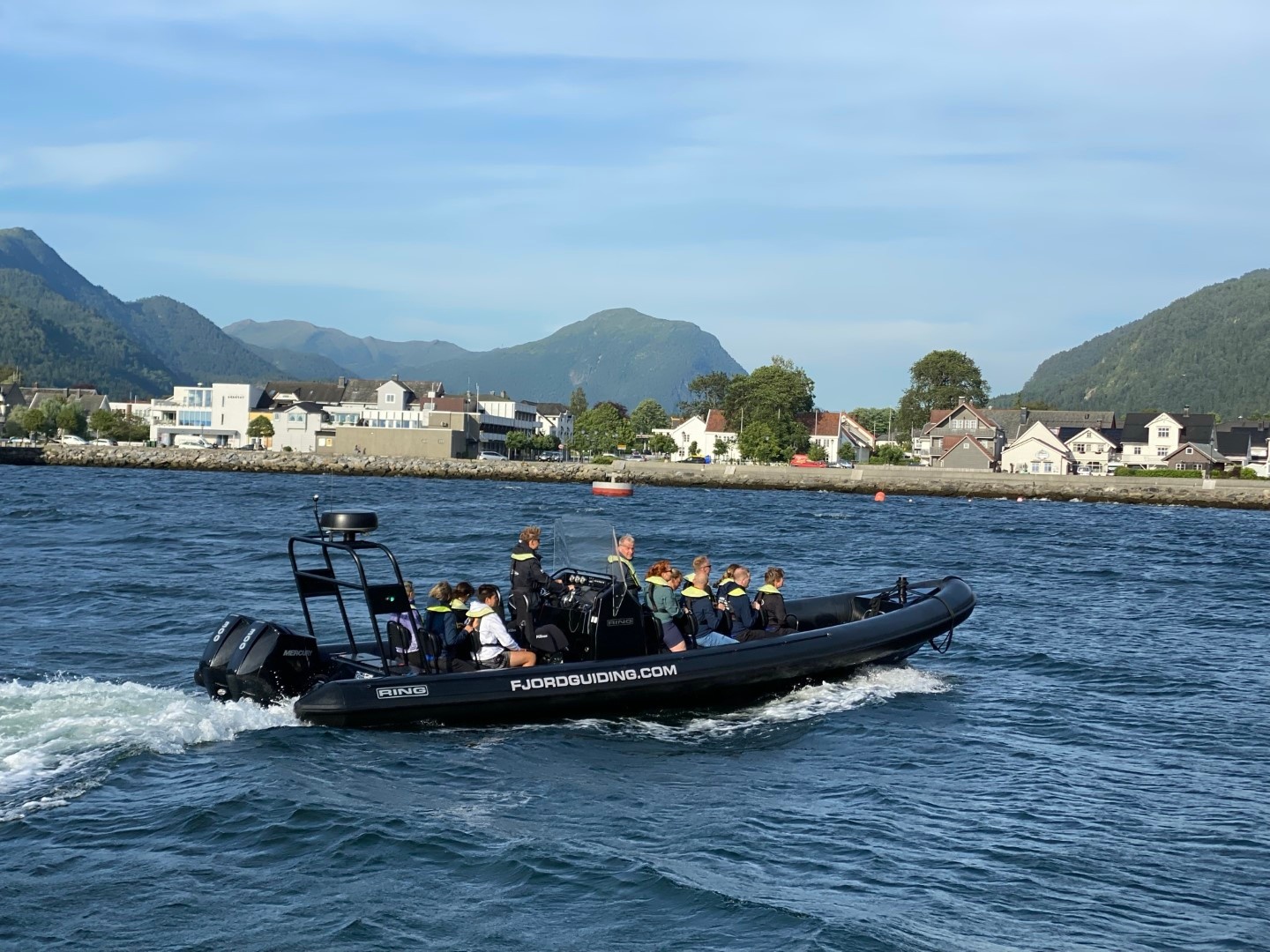 People in a speedboat on a river with mountains and houses in the background.
