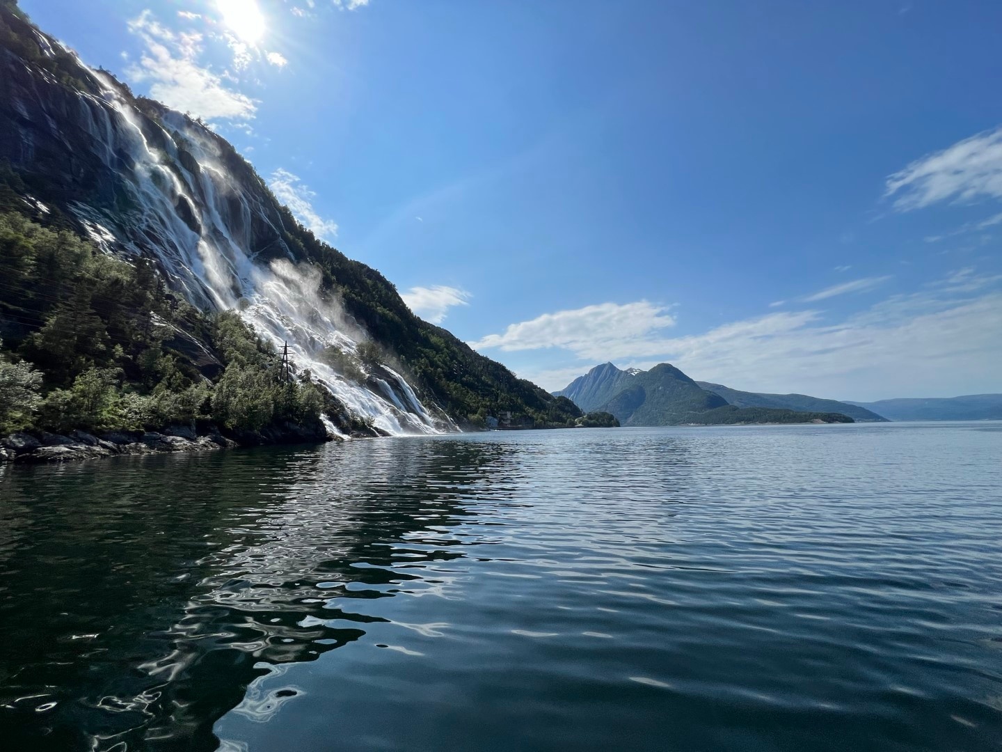 Waterfall cascading into a lake surrounded by mountains under a blue sky.
