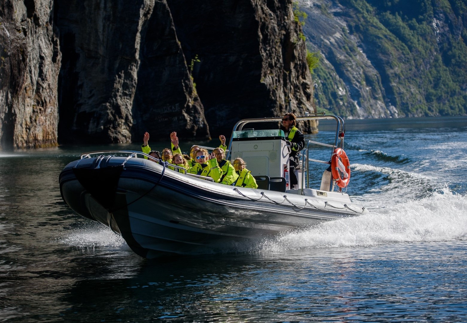 Boat with passengers in life jackets cruising through a narrow fjord.