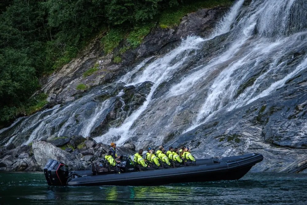 Boat with people in yellow jackets near a waterfall.