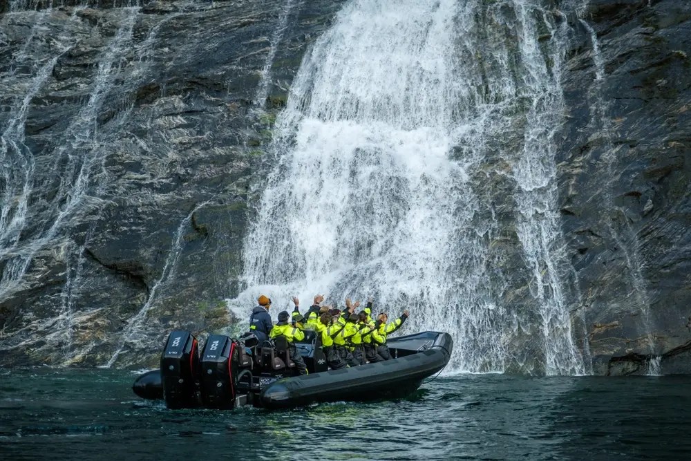 People in yellow jackets on a boat near a waterfall.